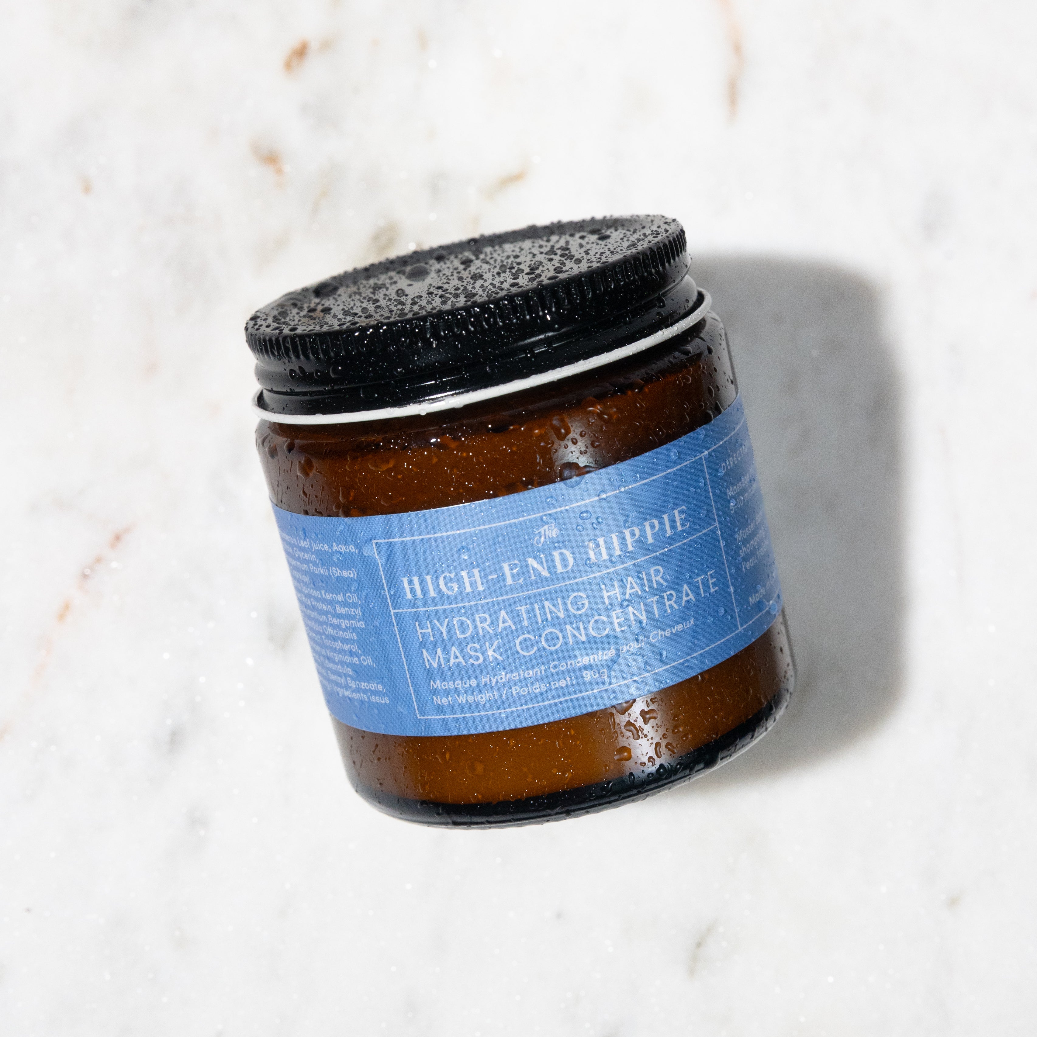 Aar of The High-End Hippie Hydrating Hair Mask Concentrate on a marble surface. Labeled callouts highlight key ingredients: horsetail (strengthens strands, reduces breakage), argan oil (restores elasticity, reduces frizz), rosemary (stimulates healthy hair growth), rice water protein (promotes hair density and body), ceramides (reinforces hair's barrier to prevent damage and color fading), and aloe (hydrates). 